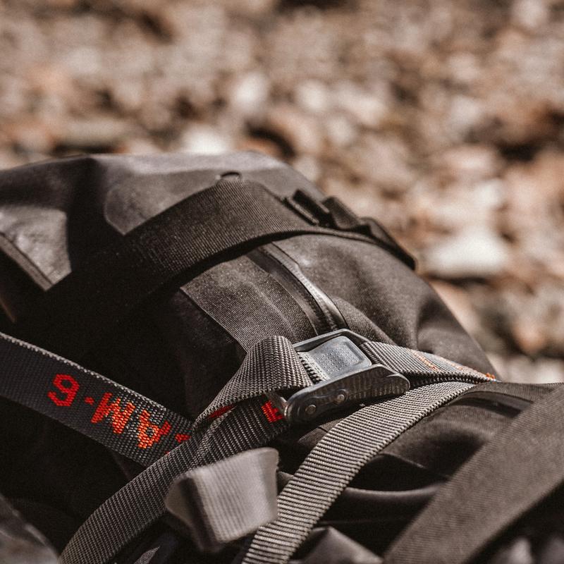 Close-up of a black backpack with Rollercam 6ft loop end straps and a blurred natural background