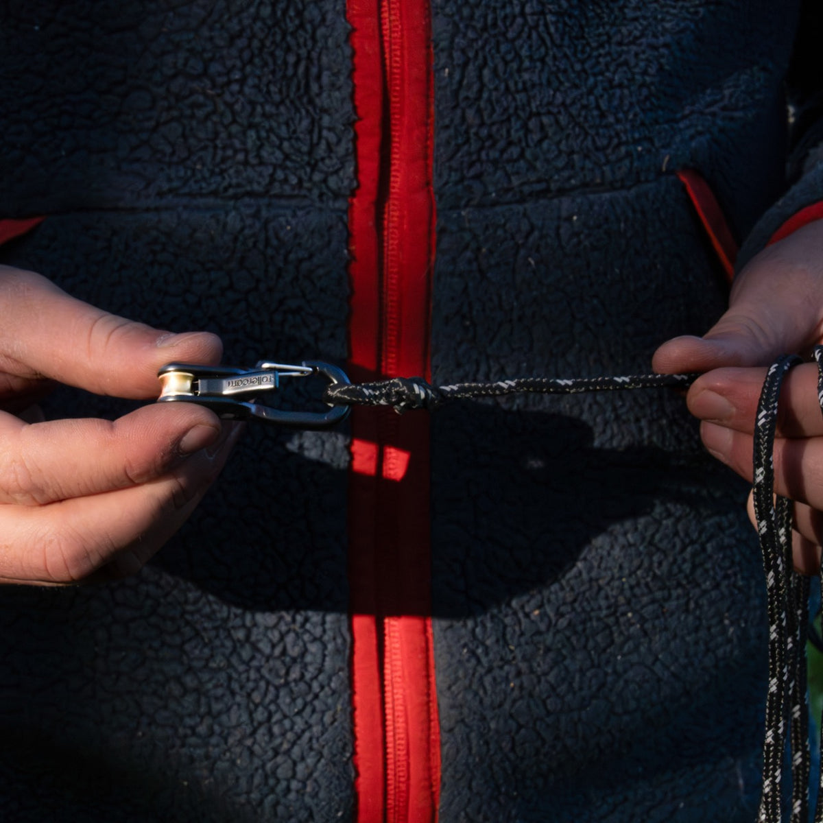 Close-up of a person's hands holding a Stealth black Roperoller attached to black accessory cord.