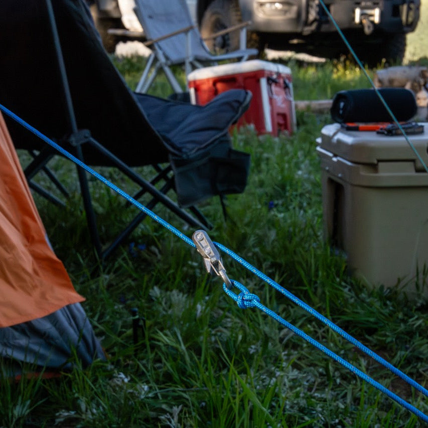 A close-up of the Rollercam Roperoller in an outdoor camping scene showing a tent, folding chair, truck, cooler, and grass in the background.