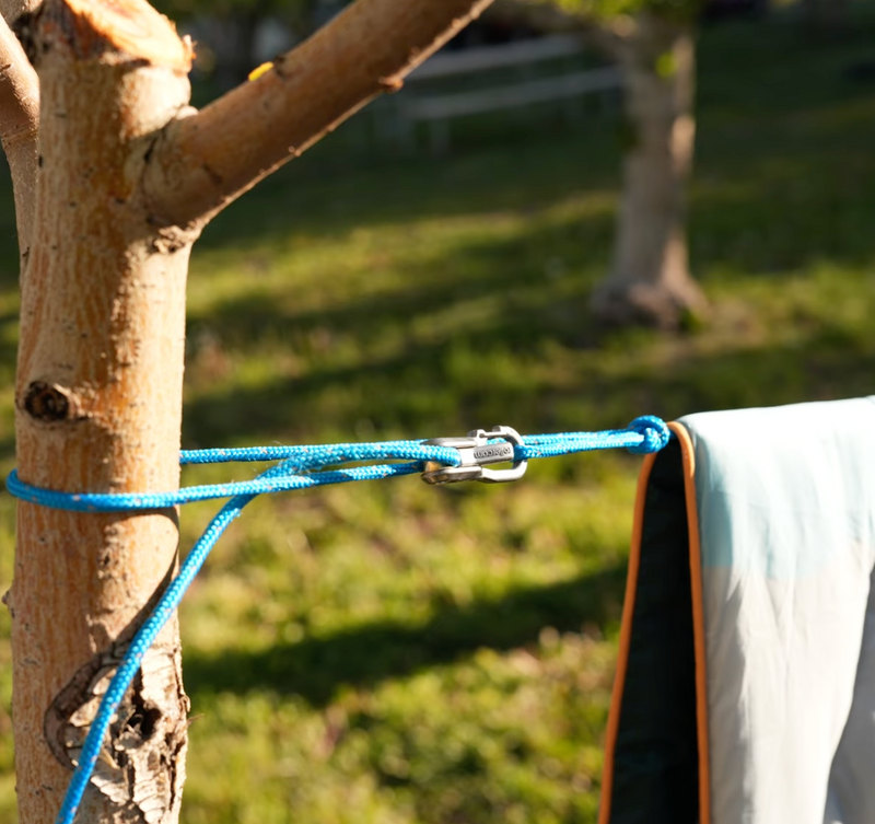 Blanket hanging on a clothesline tensioned between trees using a Rollercam Roperoller with a grassy background